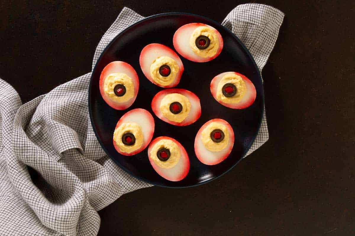Halved deviled eggs topped with olive “pupils” and paprika “veins” on a spooky tray