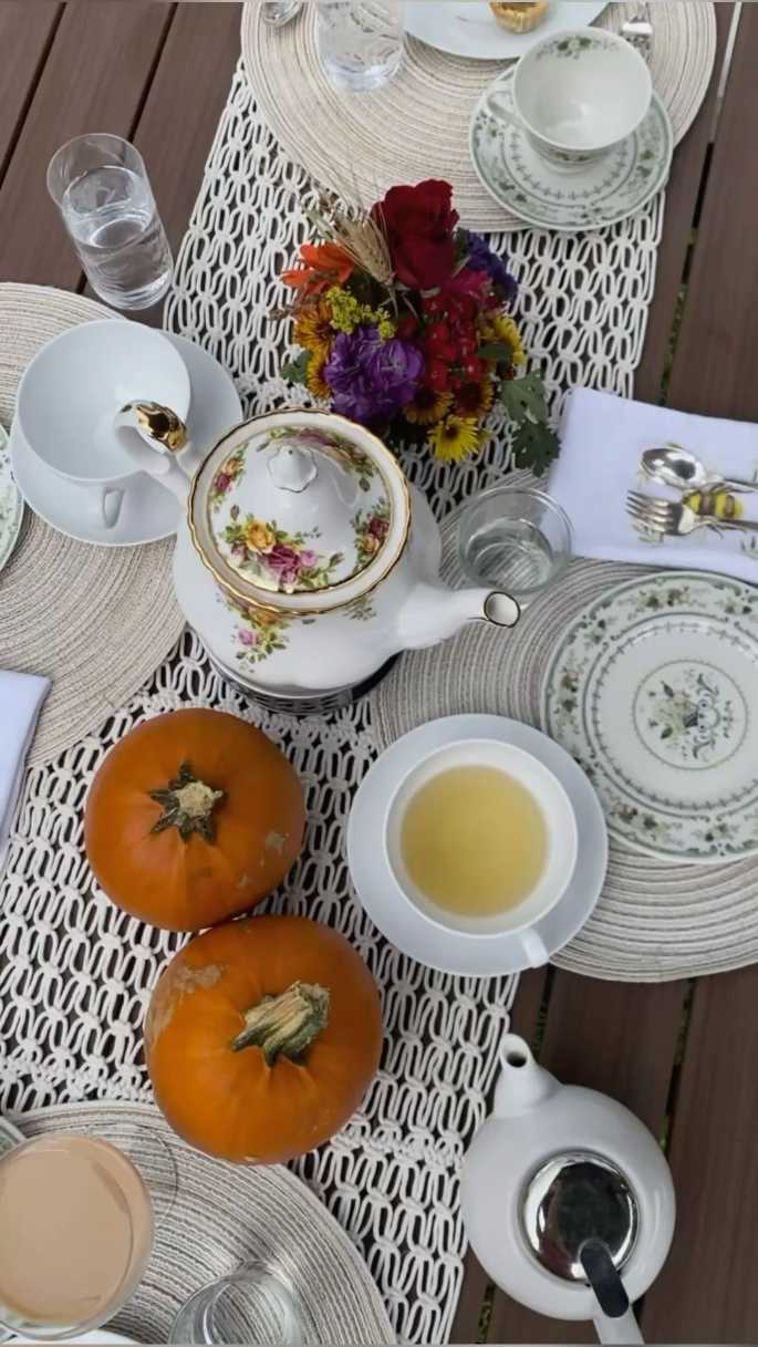 Elegant table setting with pumpkin centerpieces, golden linens, and assorted tea party pastries