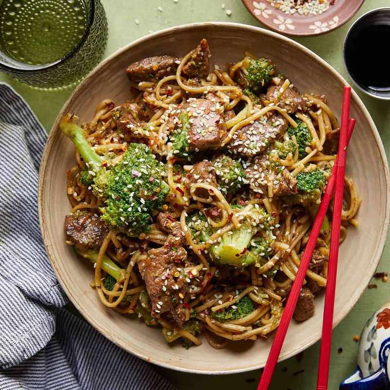 Beef and broccoli noodles topped with toasted sesame seeds, tender beef, crisp broccoli, and glossy noodles