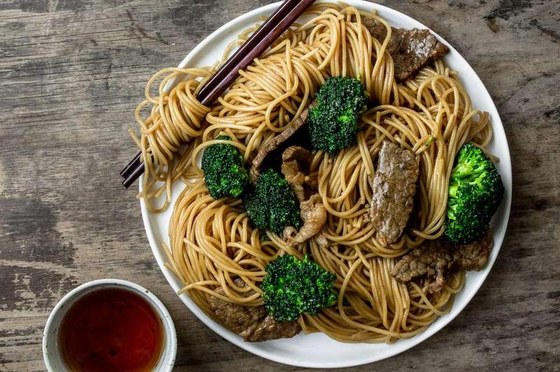 Beef and broccoli noodles with chopsticks, featuring tender beef, crisp broccoli, and glossy sauce