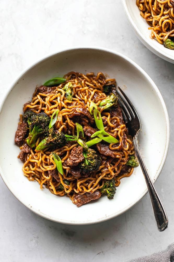 Beef and broccoli noodle plate with fork, showing tender beef, crisp broccoli, glossy sauce