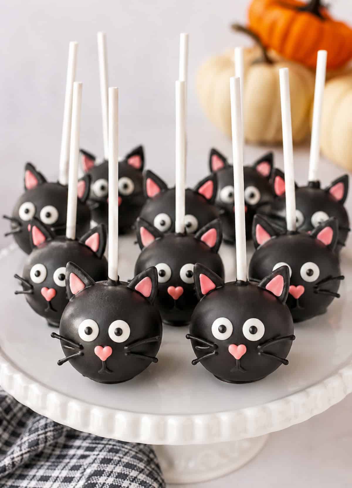 Black chocolate cake pops decorated with white icing to look like sitting cats on sticks.