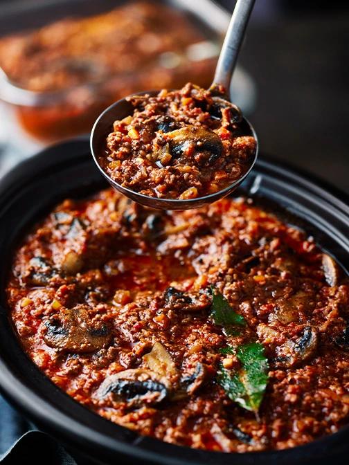 Slow cooker simmering beef bolognese with tomatoes, herbs, and a splash of red wine