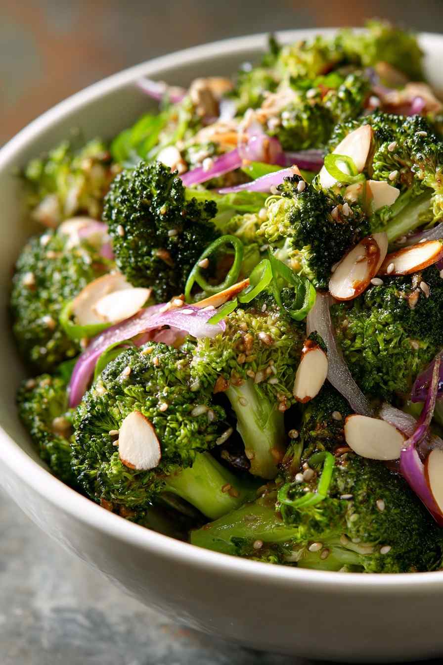 Asian broccoli salad featuring crisp florets, sesame‑soy glaze, crunchy wonton strips, sliced almonds, and scallions