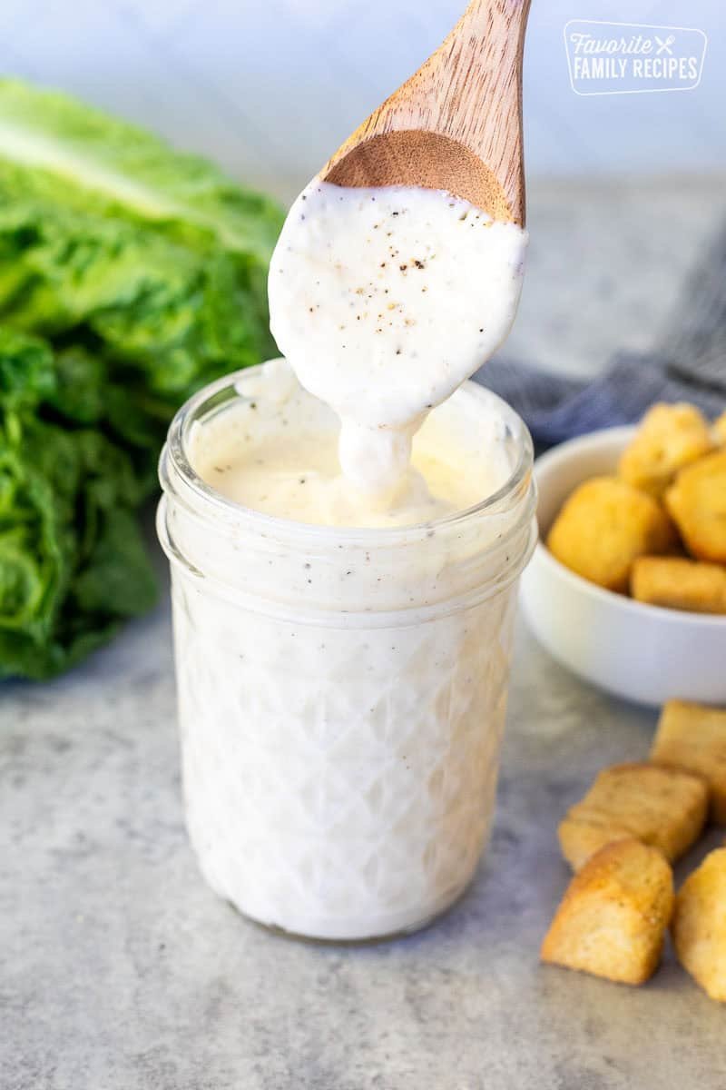 Creamy Greek yogurt caesar dressing in a bowl surrounded by fresh lemons garlic and cracked peppercorns