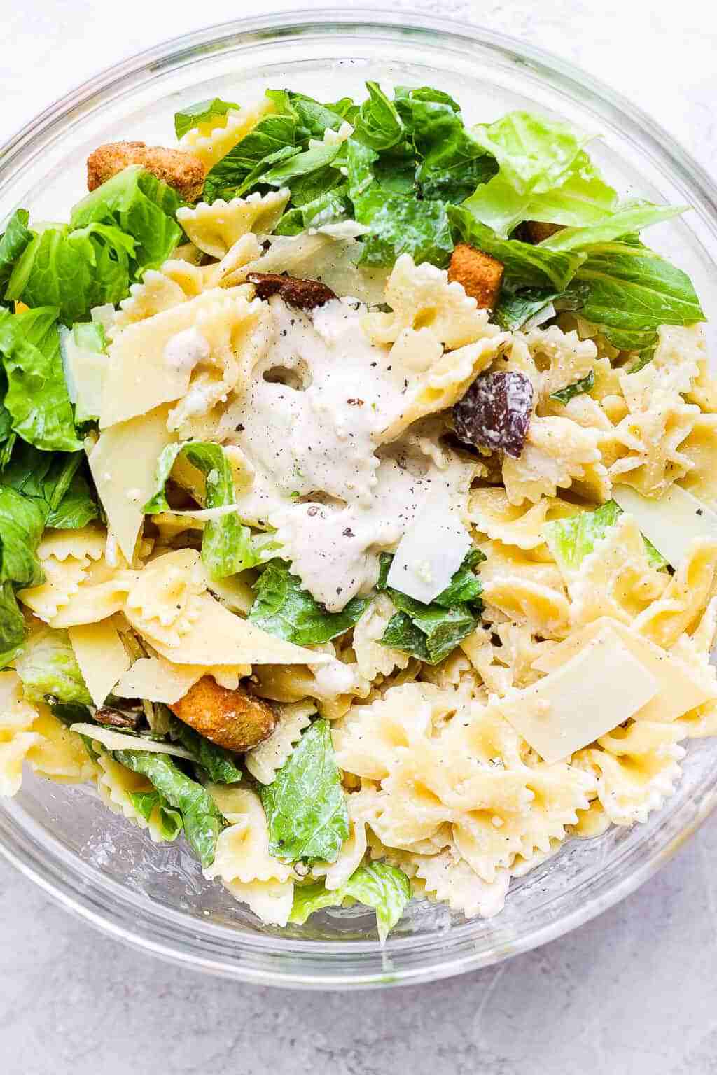 Delicious chicken caesar pasta salad featuring crisp romaine, crunchy croutons, shaved parmesan, creamy dressing.