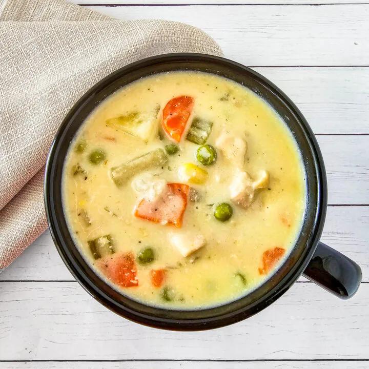 Rich chicken pot pie soup with chicken, peas, carrots, potatoes, and cheddar‑topped biscuit crumble