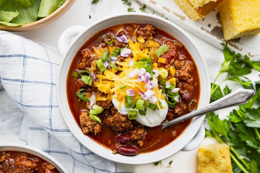 Dark rich stout beef chili in a ceramic bowl with green onions and grated cheddar