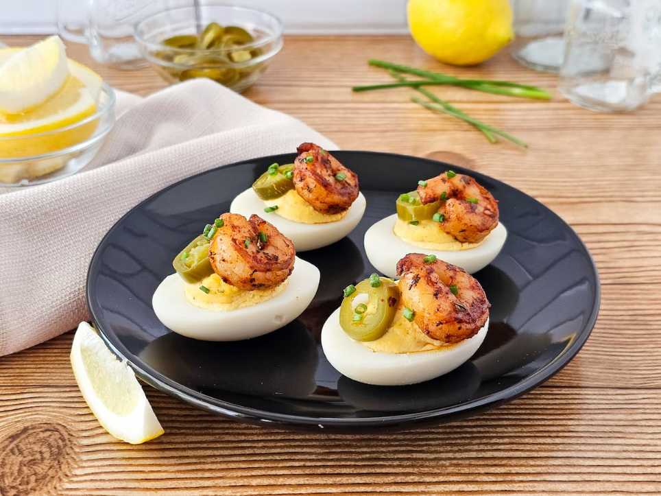 Halved deviled eggs topped with spicy Cajun shrimp and sliced jalapeño on a festive tray