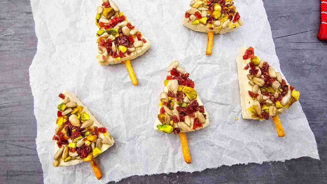 Triangular cheese wedges shaped like trees, topped with pretzel sticks as antlers on a festive platter