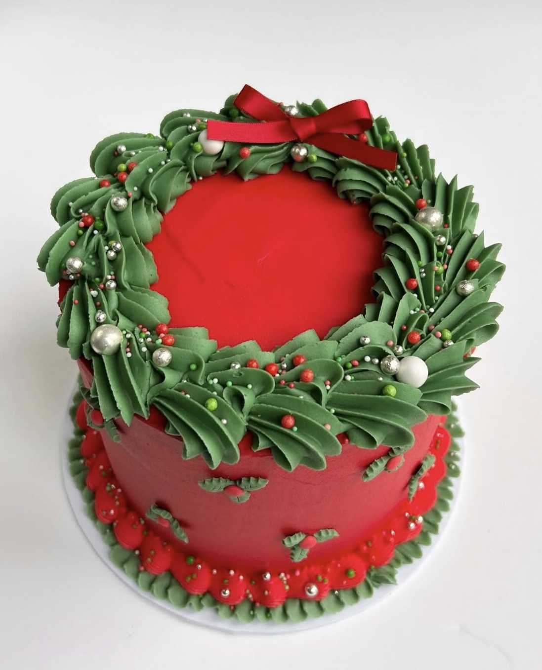 Simple vanilla cake with a glossy red buttercream wreath and silver pearl accents