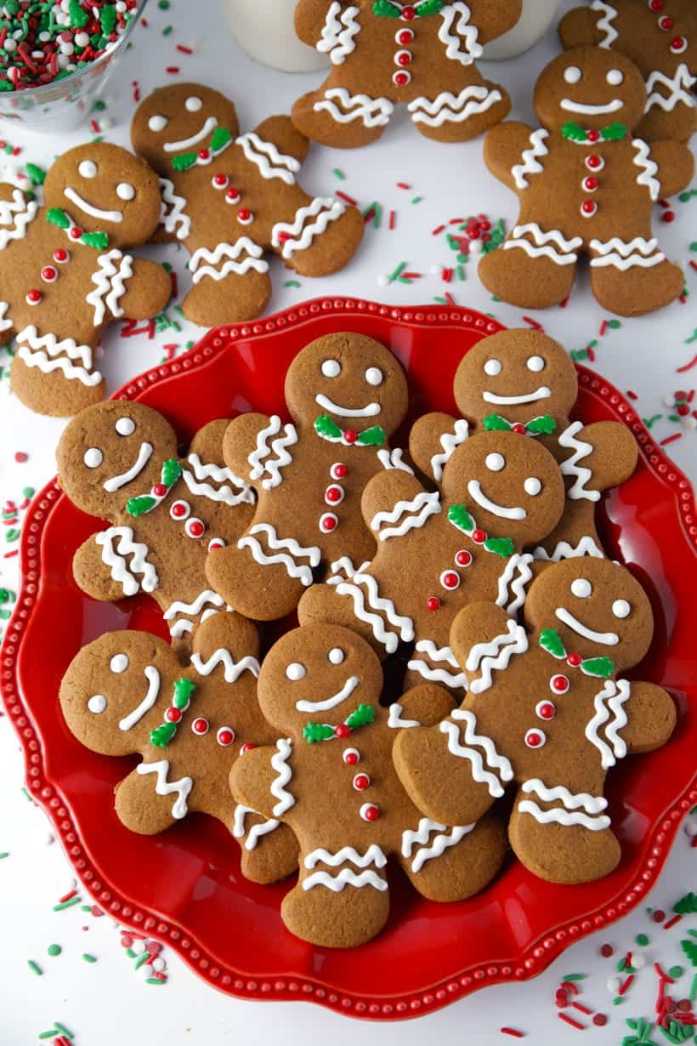 Gingerbread men cookies decorated with white icing and colorful sprinkles on a red background.