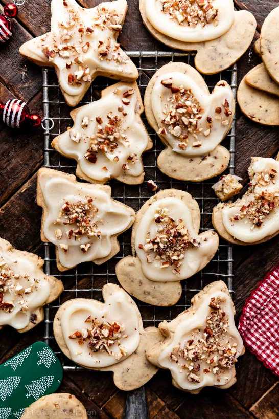 Star-shaped shortbread cookies with a white glaze and cracked pecans arranged on a white marble surface.