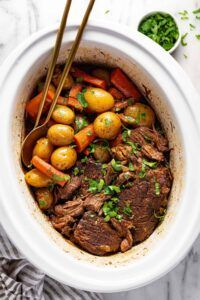 Tender beef pot roast surrounded by baby potatoes, carrots, and glossy gravy in a slow cooker