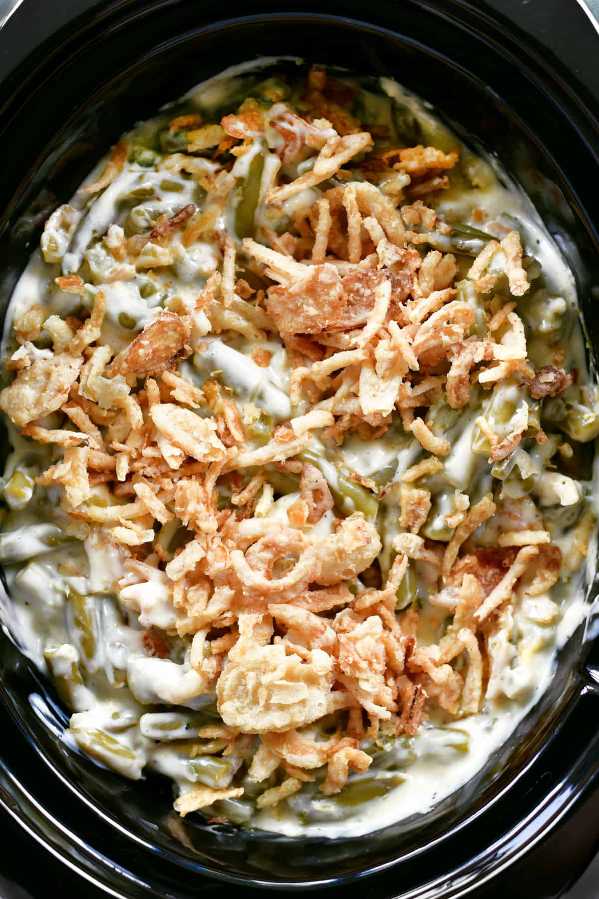 Green bean casserole topped with golden crispy onions, bubbling in a creamy sauce