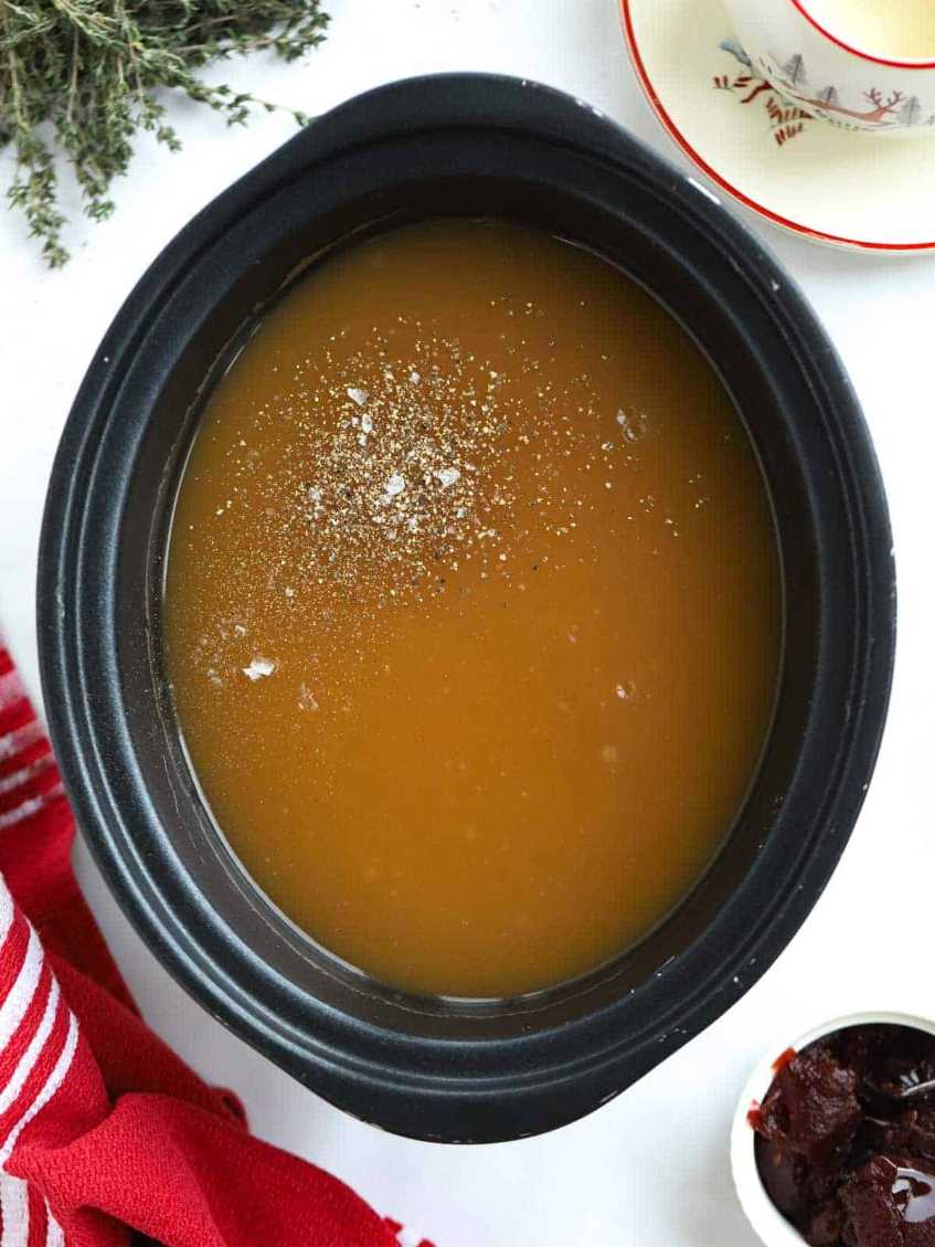Rich, glossy turkey gravy in a ramekin, speckled with fresh herbs and a drizzle of pan drippings