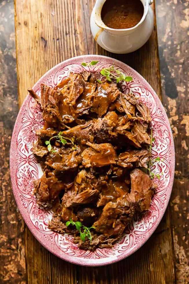 Shredded beef roast piled on a platter, drizzled with rich gravy and fresh parsley