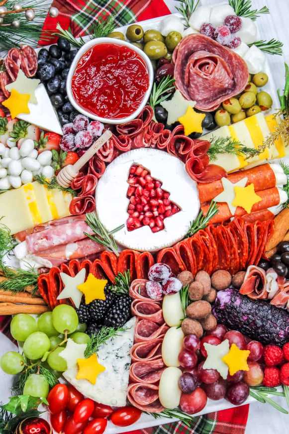 Charcuterie board shaped like a tree, featuring brie, pomegranate seeds, and cured meats