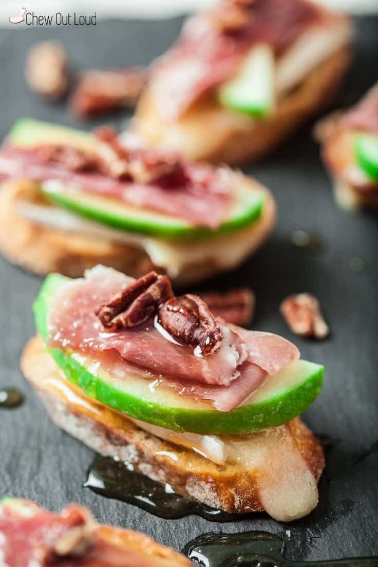 Toasted baguette slices topped with brie, apple slices, prosciutto, and honey drizzle