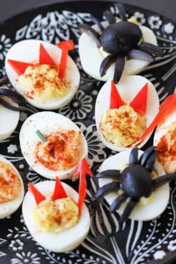 Deviled egg halves topped with olive “spiders” and a drizzle of paprika