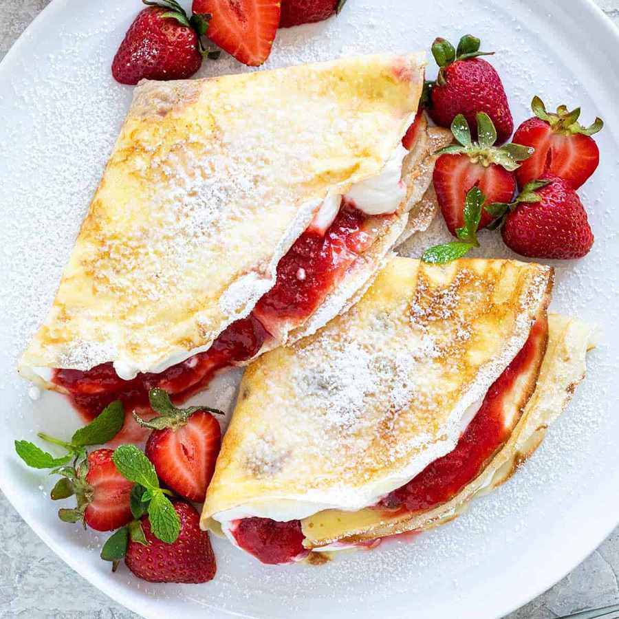 Thin golden crepes layered with strawberry‑infused whipped cream and fresh sliced berries