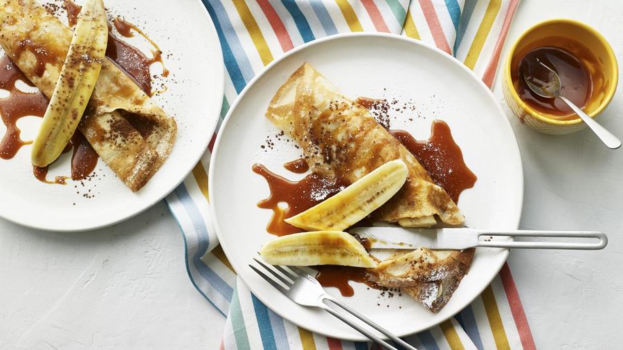Golden crepes stuffed with banana slices, drizzled with caramel sauce, topped with whipped cream