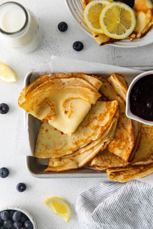 Thin golden crepes filled with lemon‑infused batter and fresh blueberries, topped with a light dusting of powdered sugar