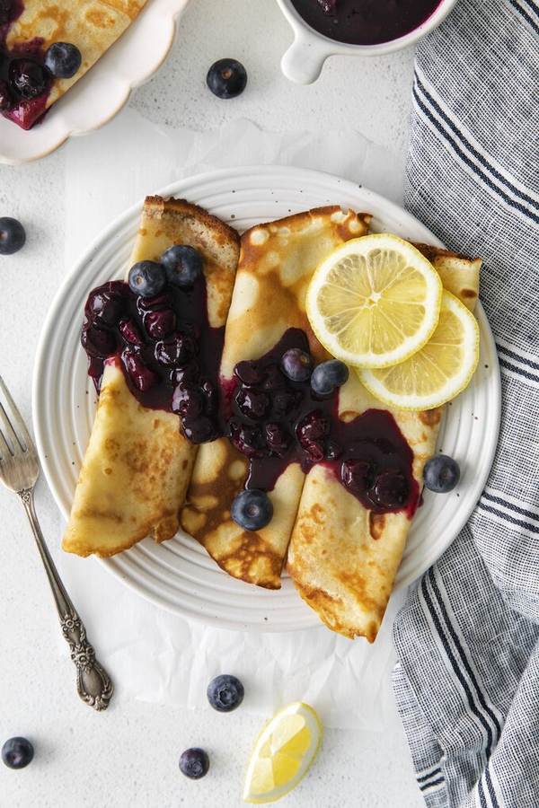 Thin golden crepes with lemon‑flavored batter and fresh blueberries, topped with a light dusting of powdered sugar