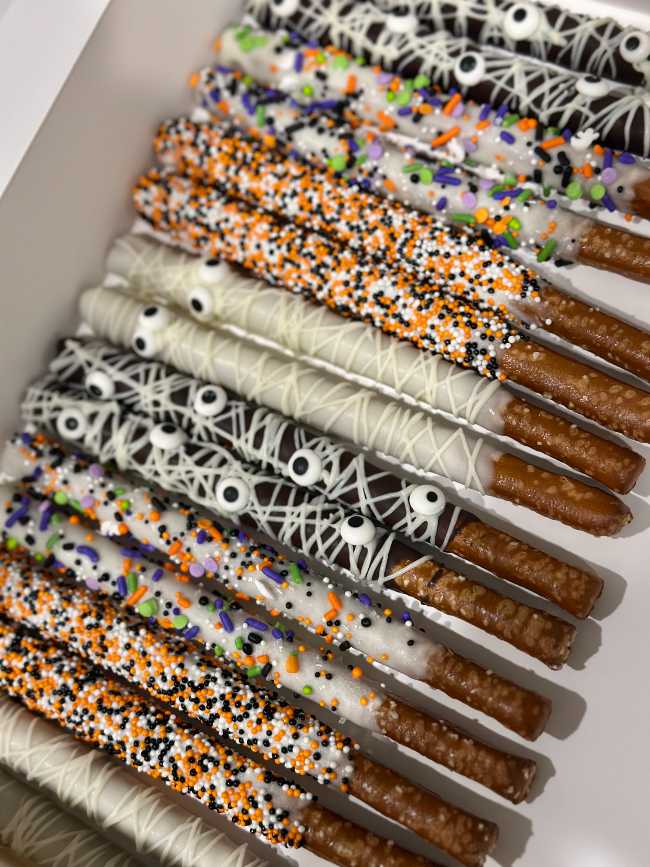 Pretzel rods dipped in white chocolate and decorated with orange and purple sprinkles.
