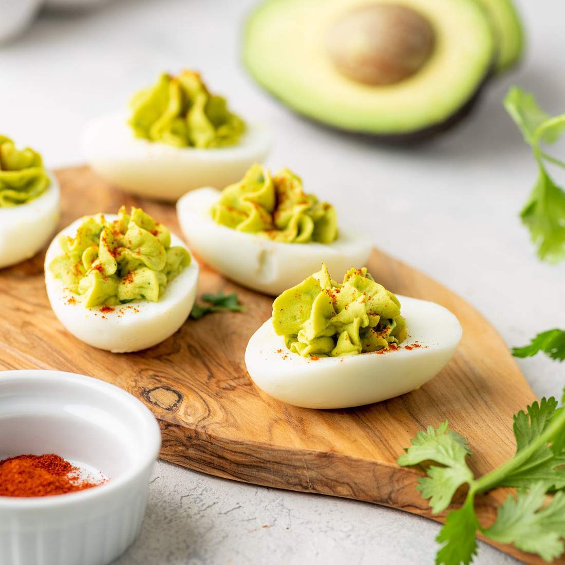 Lime‑avocado deviled eggs, creamy filling, crisp bacon bits, chives, paprika dust