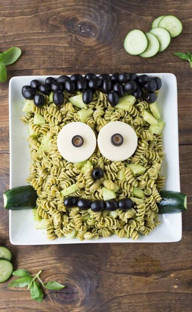 Green pesto pasta tossed with cherry tomatoes, mozzarella “eyes,” and black olive “scar” lines on a Halloween platter.