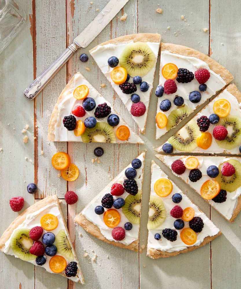Sugar cookie fruit pizza topped with cream cheese frosting, sliced peaches, strawberries, and blueberries
