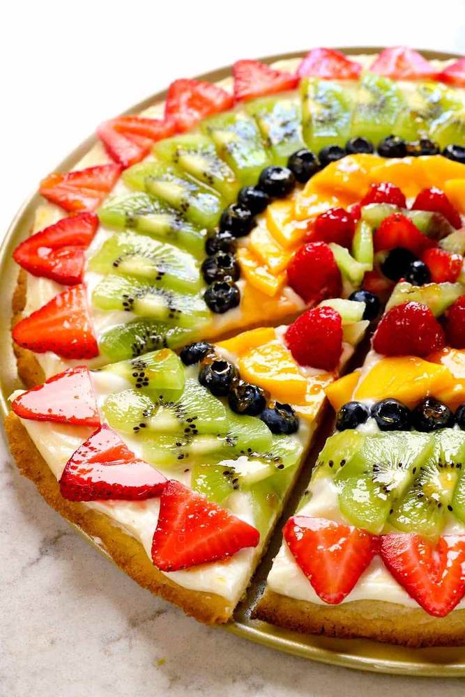 Sugar cookie fruit pizza topped with cream cheese frosting, caramel drizzle, sliced apples, and blueberries