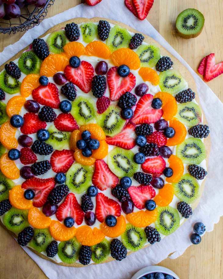 Sugar cookie base with cream cheese frosting topped with fresh mango, pineapple, and passion fruit, tropical fruit pizza delight