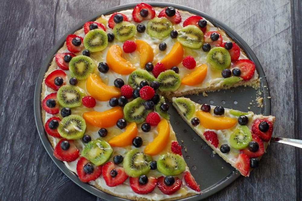 Sugar cookie base with lime‑zest cream cheese frosting, sliced kiwi, and a dusting of powdered sugar, refreshing fruit pizza