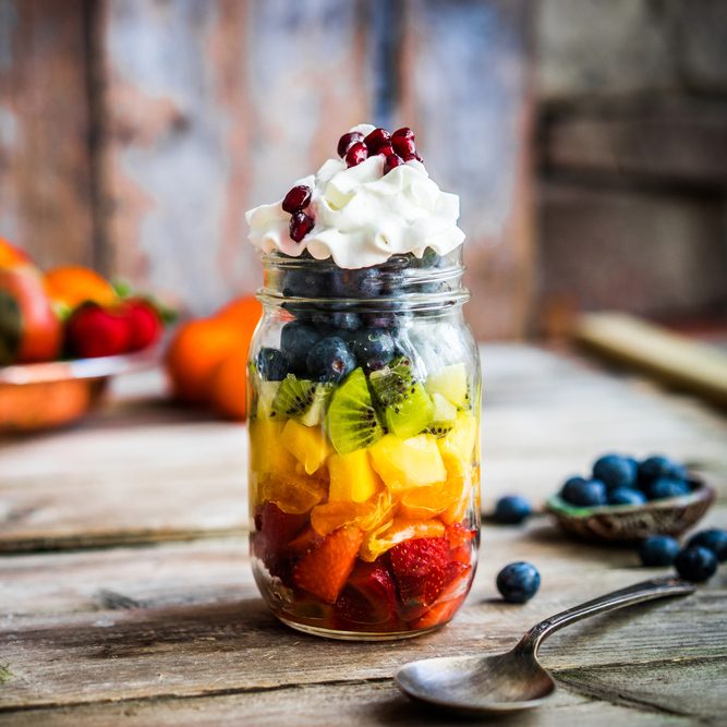 Vibrant layered fruit cups in jars with berries, citrus segments, and a light honey‑lime drizzle