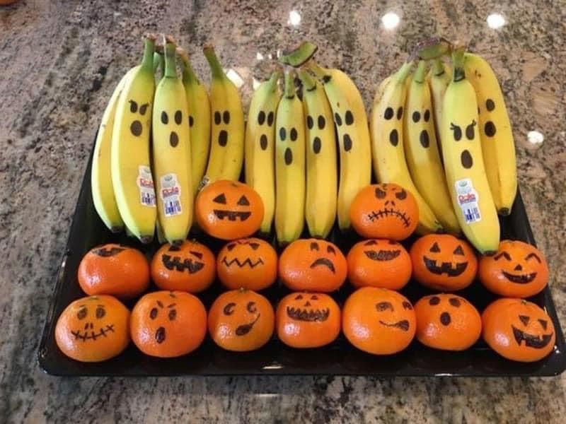 Banana halves with white chocolate “ghost” faces and clementine “pumpkin” wedges arranged on a spooky fruit platter.