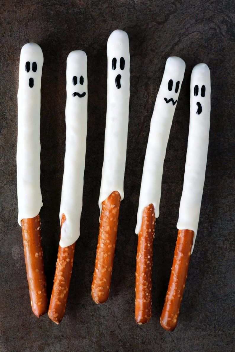 Crunchy pretzel rods dipped in white chocolate, topped with black candy eyes, forming ghostly shapes.