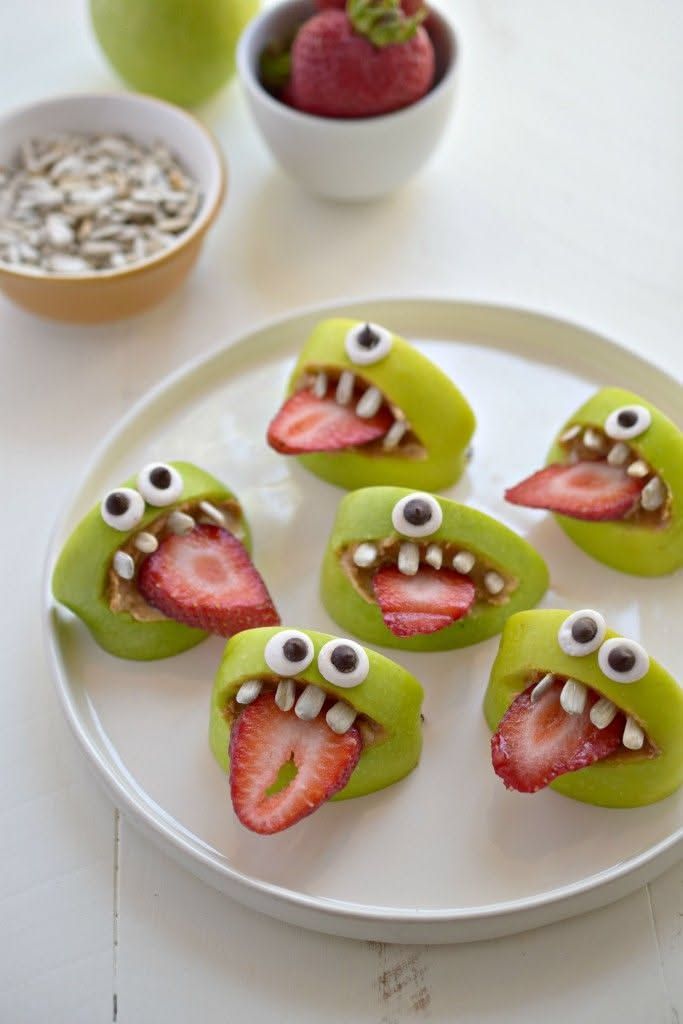 Halved green apples scooped, filled with strawberry puree and sprinkled with pumpkin‑like seeds, forming monster mouths.