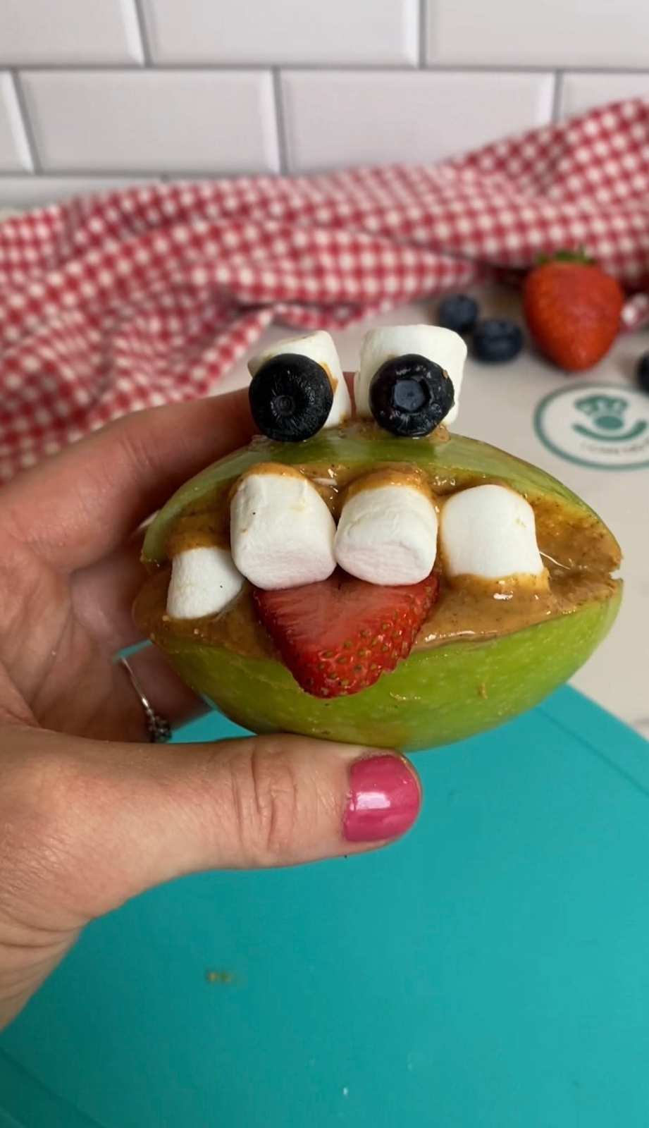 Green apple halves spread with peanut butter, topped with sliced strawberries as “teeth” and chocolate eyes.