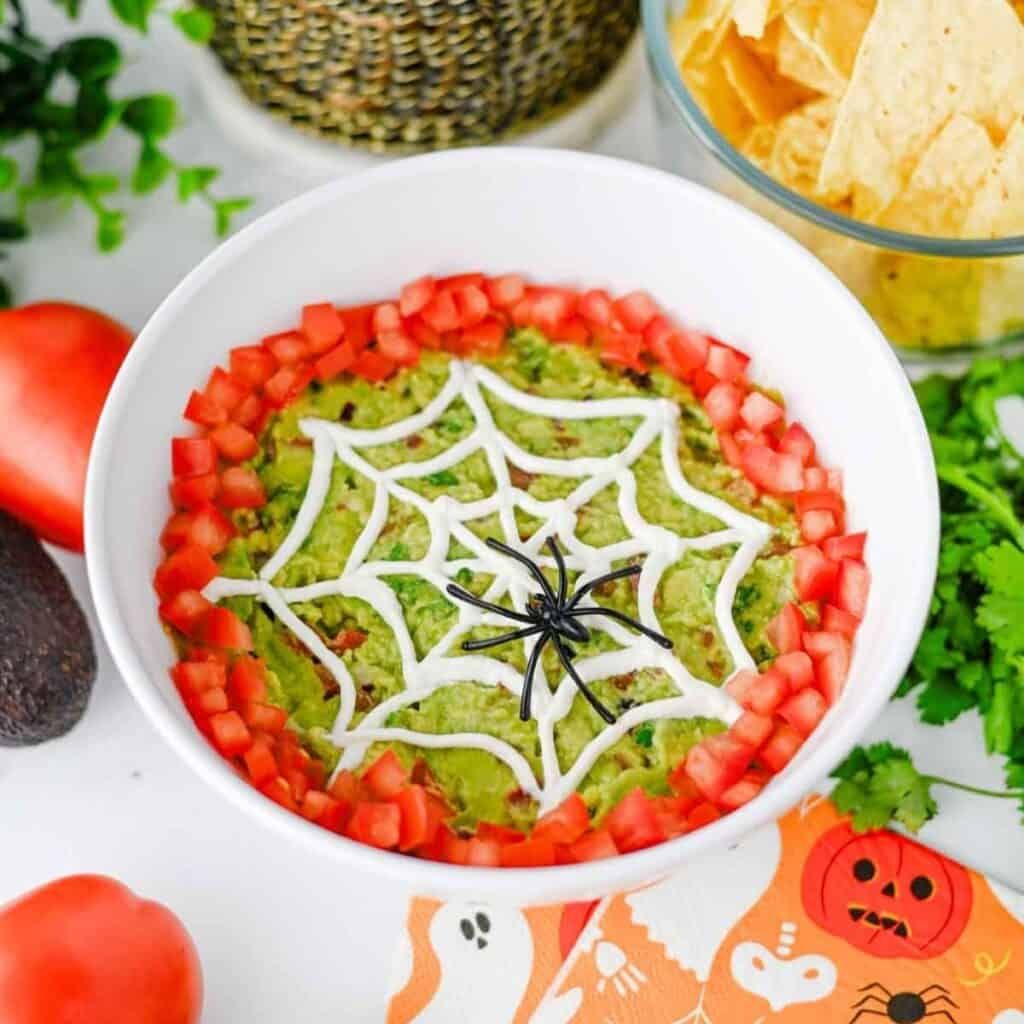 Dark green guacamole swirled with black olive “spider” garnish, served with tortilla chips.