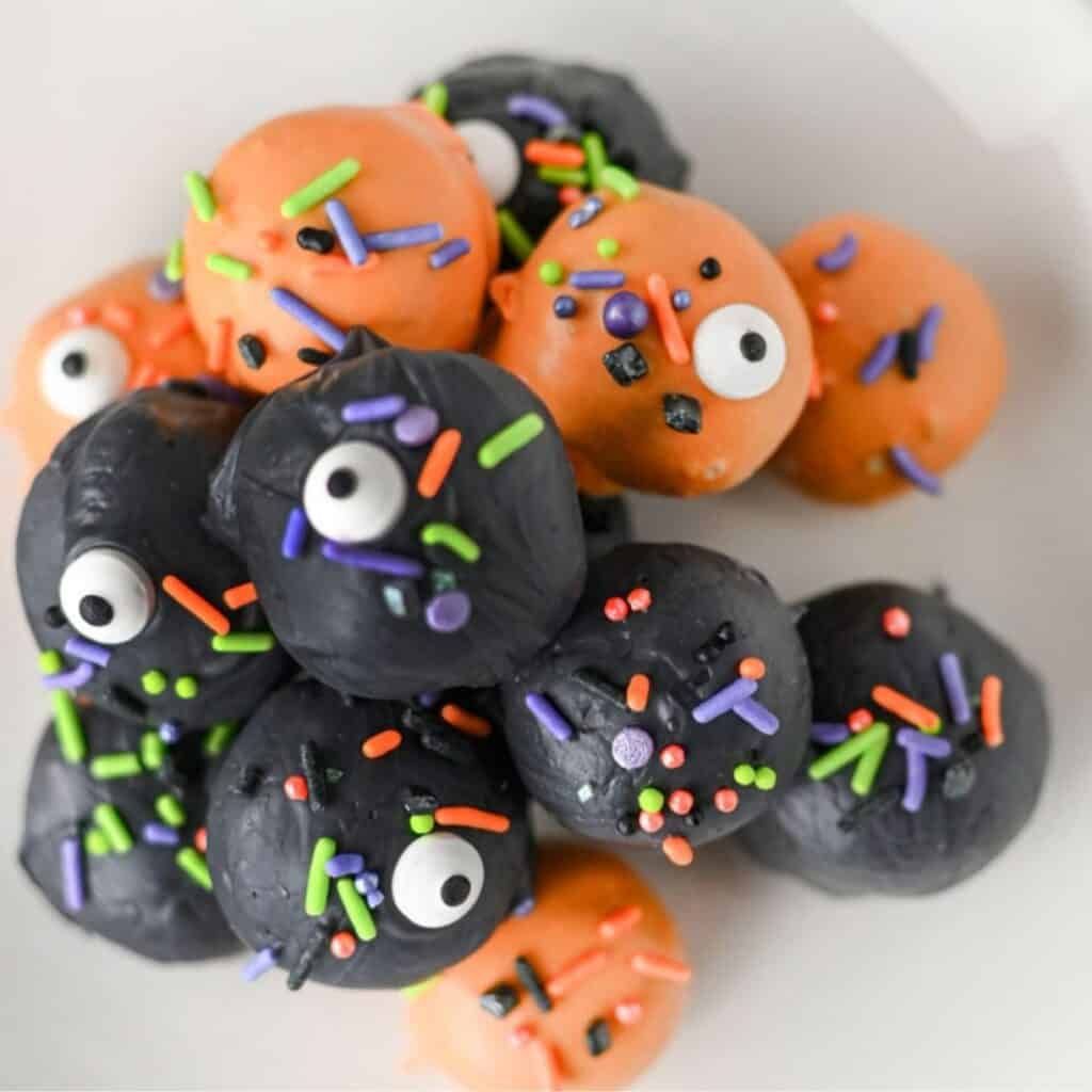 White chocolate‑coated Oreo balls with dark chocolate “eyes” perched on a parchment sheet.