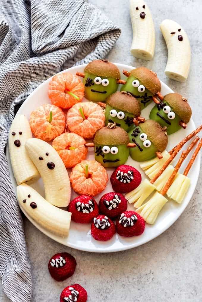 A vibrant platter of sliced bananas, clementine wedges, kiwi “ghosts,” and strawberry “pumpkin” slices arranged in a spooky pattern.