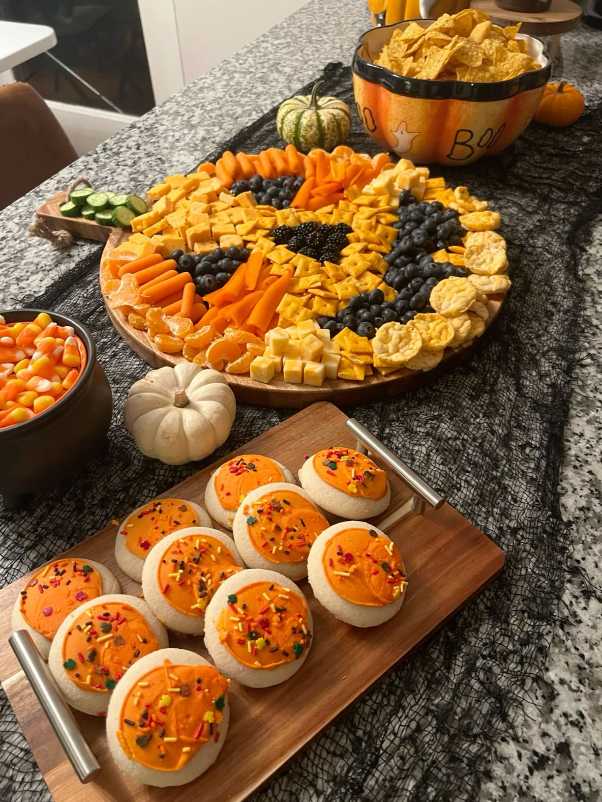 A cheese board with jack-o-lantern shapes and frosted cookies.