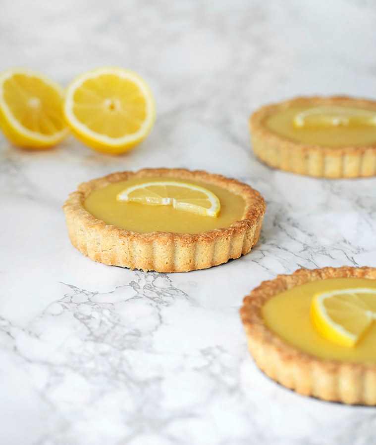 Elegant lemon curd tart with a glossy top, bright yellow, on a rustic wooden board, garnished with berries