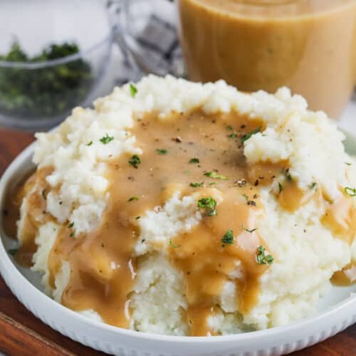 Creamy buttery mashed potatoes with gravy, roasted garlic, melted cheese, and chives in warm bowl