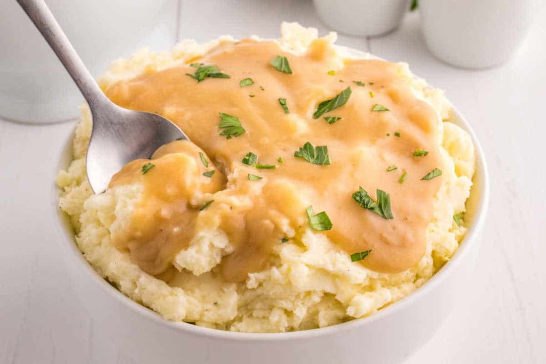 Creamy buttery mashed potatoes with gravy, melted cheese, roasted garlic, and chives in warm bowl