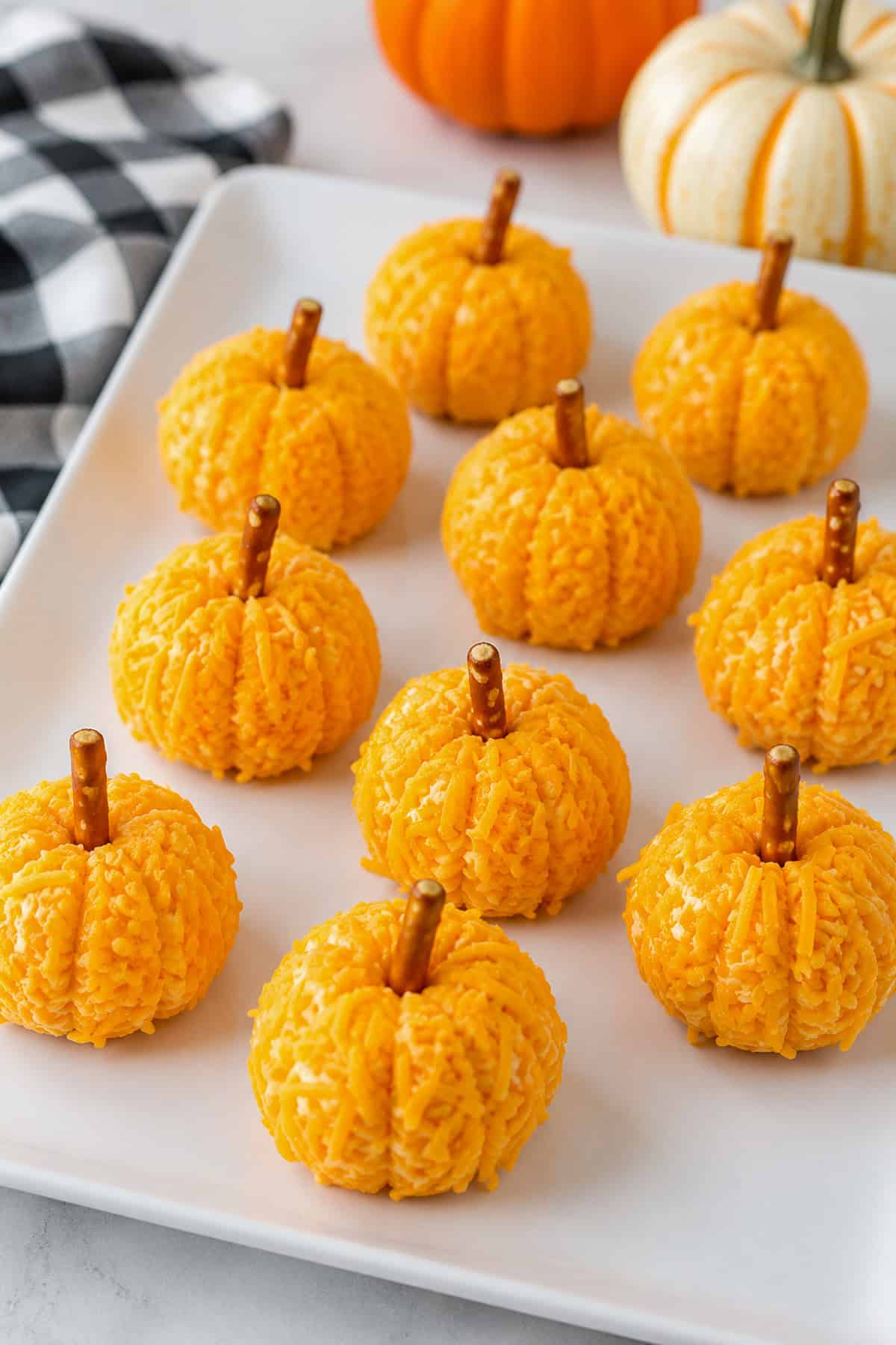 Orange cheese balls rolled in orange sprinkles shaped like pumpkins with mini pretzel stems on a white plate.