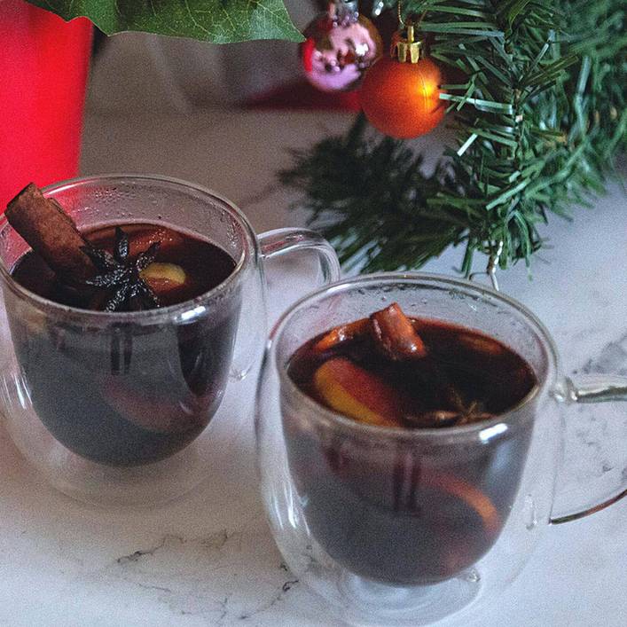 Homemade spiced mulled wine garnished with cracked cardamom pods and fresh orange peel in rustic mug