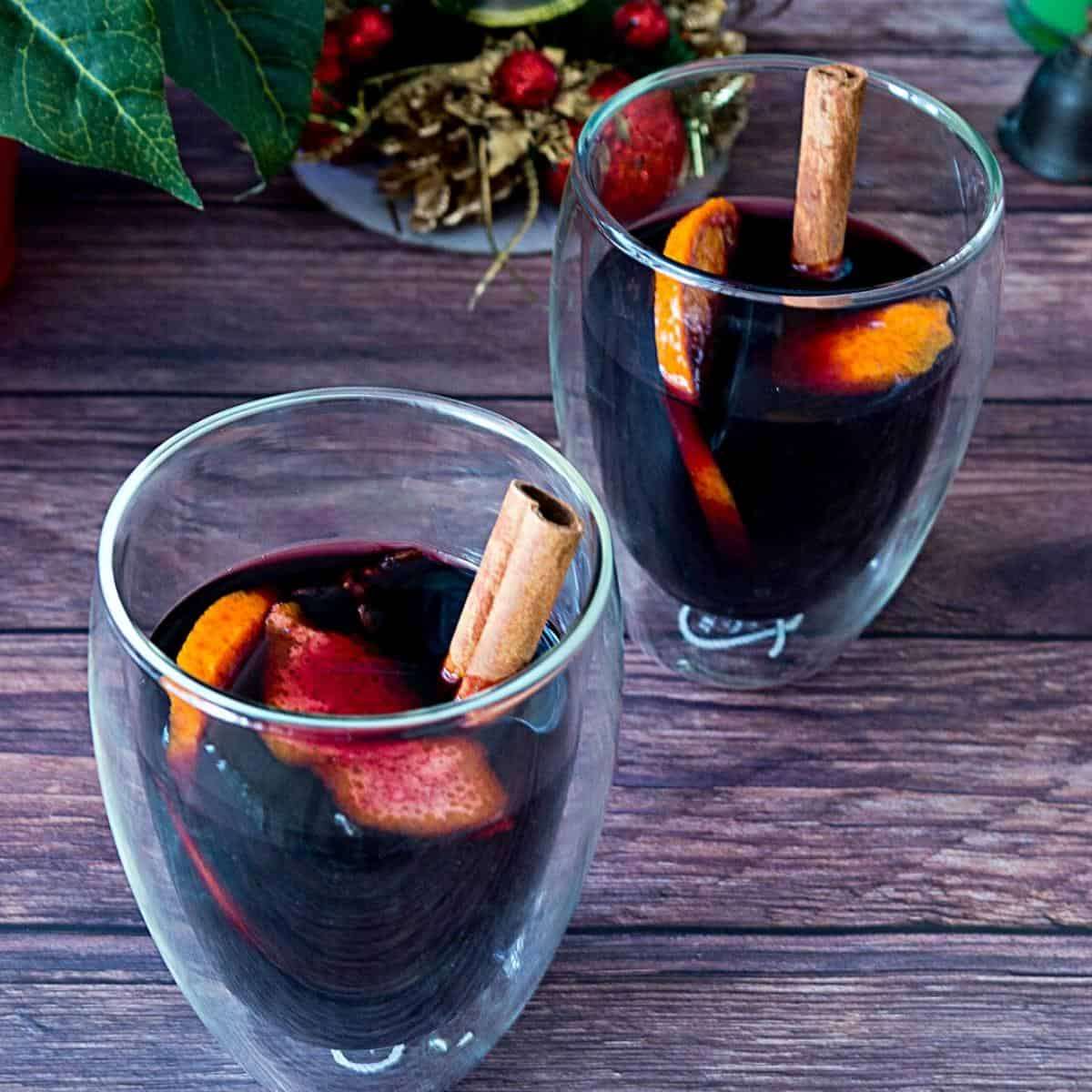 Homemade spiced mulled wine featuring deep ruby-red wine, studded orange slices, and cinnamon sticks in mugs.